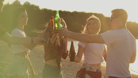 Five-students-celebrate-a-birthday-on-the-open-air-party-with-beer-and-good-mood.-They-drink-beer-and-dance-in-the-summer-evening-near-the-lake-coast.-This-is-carefree-party-at-sunset.